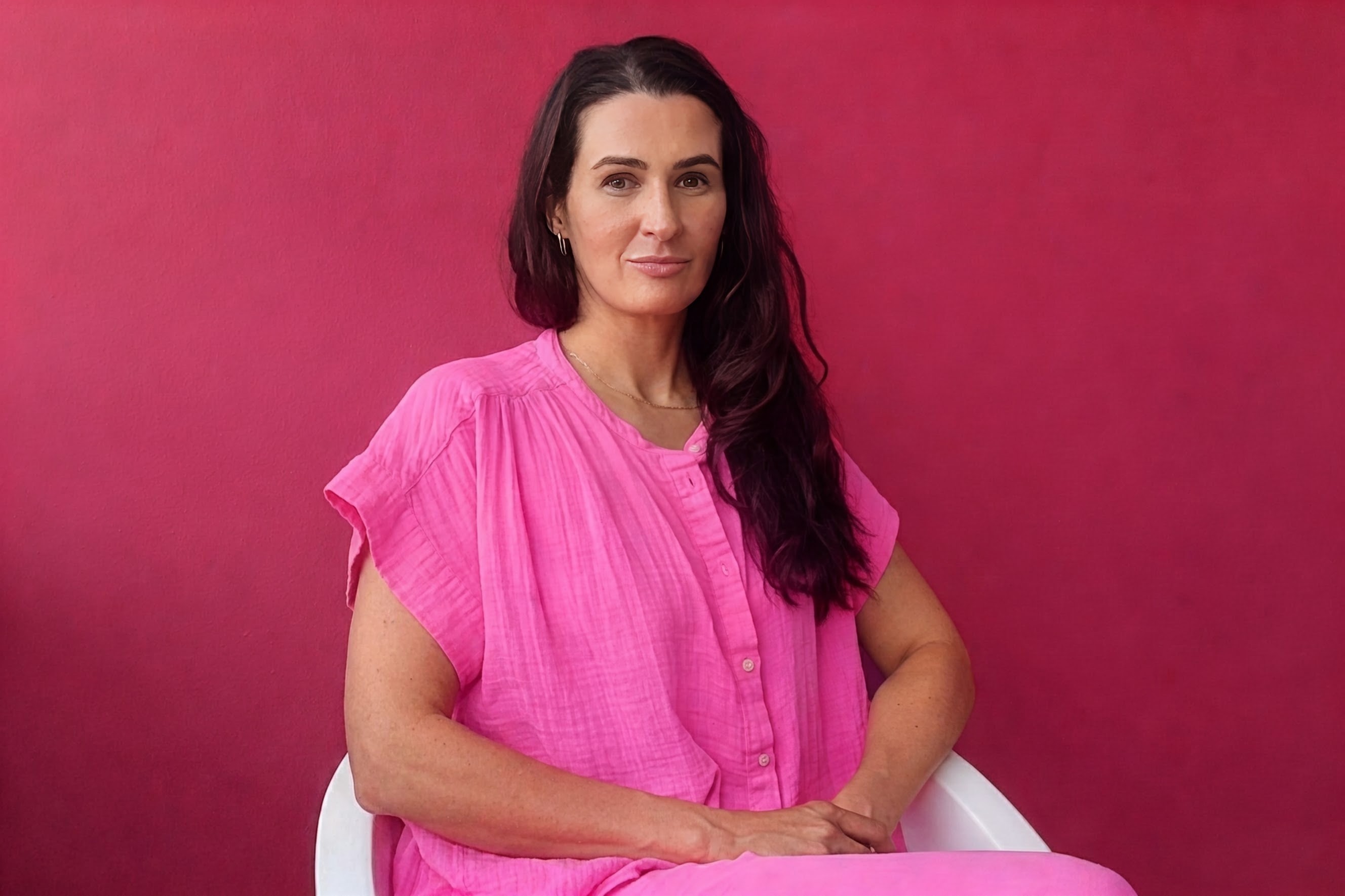 Bridget Hanna, seated against a raspberry-pink wall, wearing a pink blouse